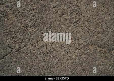 The scene shows a close view of a concrete surface with visible cracks. Small stones are embedded in the rough texture. Sunlight brightens the outdoor Stock Photo
