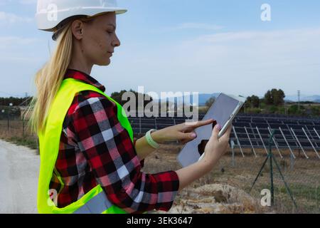 Woman engineer using a digital tablet for data analysis and management, ensuring efficient operations and maintenance of a solar power station while p Stock Photo