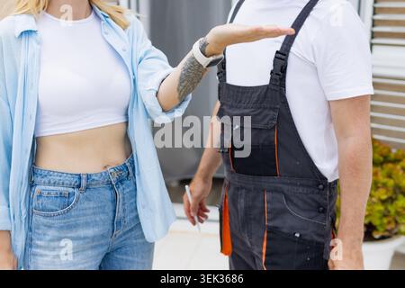 Woman engaging in a professional consultation with a repairman, gesturing with her hand while discussing services and terms for a home maintenance or Stock Photo