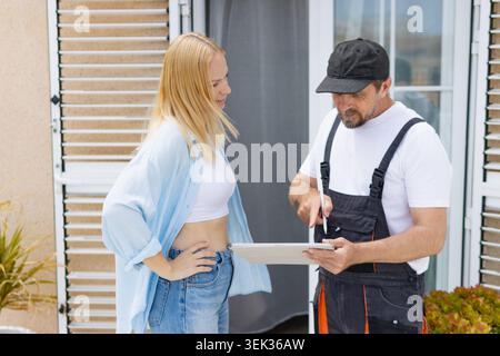 Professional handyman consulting with a woman homeowner, presenting a digital work estimate and discussing renovation plans using a tablet for efficie Stock Photo