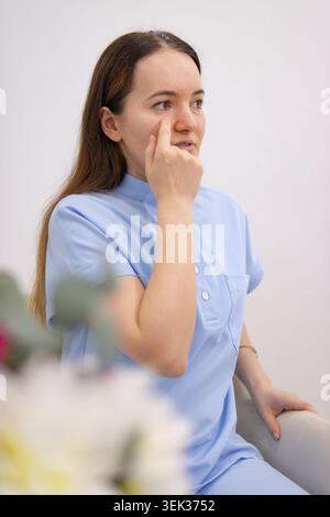 Woman in medical uniform demonstrating eye care, pointing to her under-eye area for beauty, skincare, and cosmetic procedure concepts, showing self-ca Stock Photo