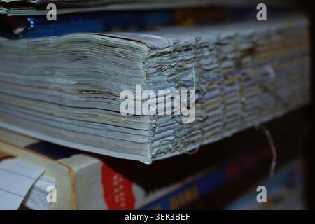 Layers of heavily used and aged paper visible from the side of a stack of books or magazines, showing frayed edges, faded colour, and texture. Stock Photo