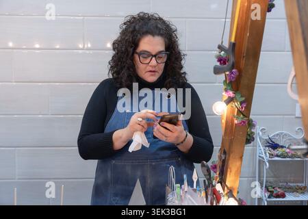 Busy woman wearing an apron and glasses, managing her artisanal products business Stock Photo