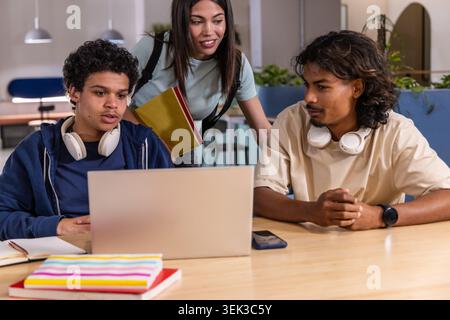 Diverse students studying in campus lounge with silver laptop white headsets yellow red notebooks Stock Photo