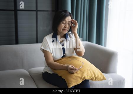 Mature Asian woman having migraine headaches at home with health concerns Stock Photo