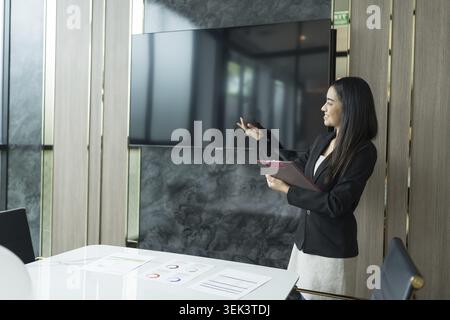 Beautiful Asian businesswoman in black suit showing at the presentation screen how a digital entrepreneur presents a project on a blank blank screen, Stock Photo