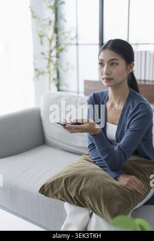 Asian woman watching smart TV and using the remote control, hand holding the television, the audio remote control at home with the remote controlled t Stock Photo
