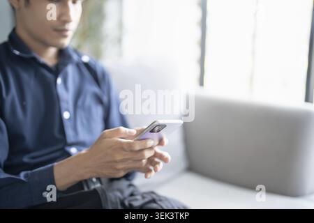 Relaxed young Asian man using smartphone and spending time checking messages on social media Stock Photo