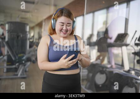 Woman using smartphone after working out at gym. Overweight Asian woman watches online workout training Stock Photo