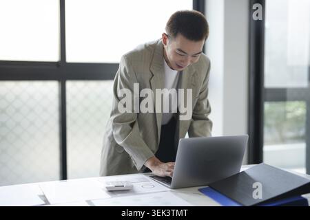 Attractive, self-confident Asian businessman from Generation Y with laptop and professionally working investor, start-up project, business planning in Stock Photo