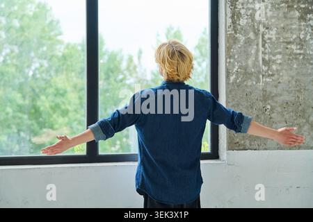 Young man standing back to camera with arms raised Stock Photo