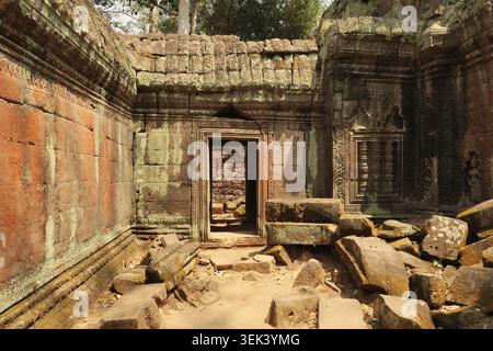 Inside one of the courtyards of the Ta Prohm Temple, the walls are covered with red and green moss, lichens, big stones, bricks on the ground, Angkor Stock Photo