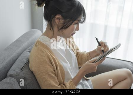 Asian businesswoman working from office taking notes to read and write in notepad Stock Photo