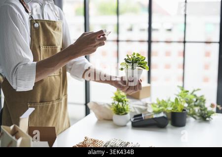 Asian male small business owner from an environmentally friendly plant shop uses smartphone to live stream and promote sustainable green online using Stock Photo