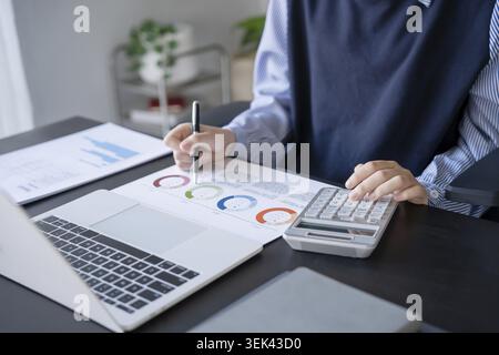 Asian businesswoman doing paperwork with pen, laptop calculator Stock Photo