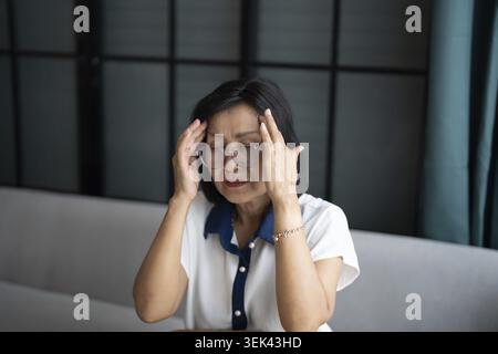 Mature Asian woman having migraine headaches at home with health concerns Stock Photo