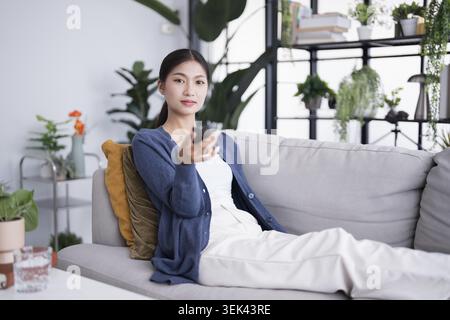 Asian woman watching smart TV and using the remote control, hand holding the television, the audio remote control at home with the remote controlled t Stock Photo