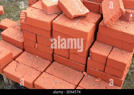 Red ceramic bricks stacked on a wooden pallet at a construction site. High-quality clay building blocks, ready for wall construction, home renovation, Stock Photo