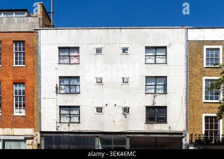 The symmetrical facade of a white multi story building with multiple small windows situated between brick houses. Stock Photo