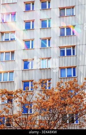 Abstract background of a multi story apartment building wall with ribbed texture, window rows and colorful fall foliage Stock Photo