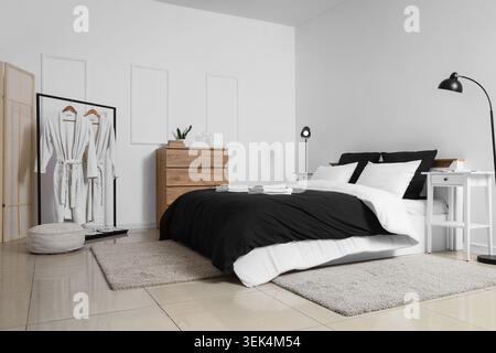 Interior of hotel room with clean linen on bed, lamps and bathrobes Stock Photo