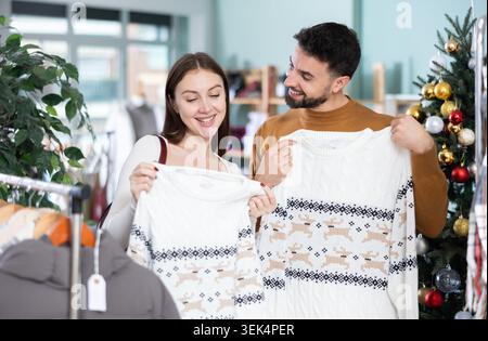 Couple choosing a warm sweater against the background of a Christmas tree in a decorated store Stock Photo
