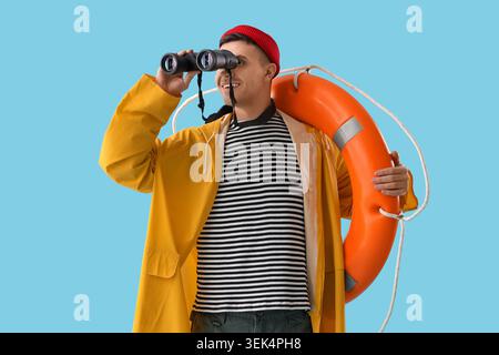 Young sailor with ring buoy looking through binoculars on blue background Stock Photo