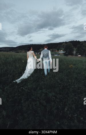 Couple walks hand in hand through tall grass Stock Photo