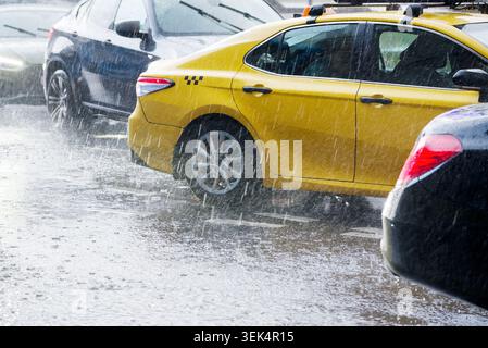 Yellow taxi cab driving through heavy rainfall on a flooded city street during a summer downpour Stock Photo