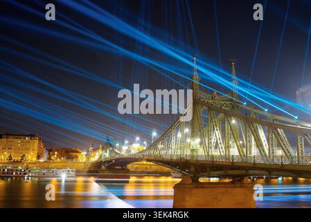 Liberty Bridge in Budapest illuminated at night with bright blue laser beams shooting into the sky during a festival light show over the Danube Stock Photo