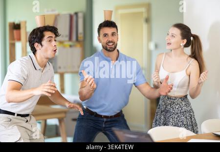 Office workers balancing cups on head enjoying their break time Stock Photo