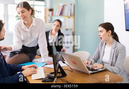 Young woman flirting with male colleague while sitting on office desk Stock Photo
