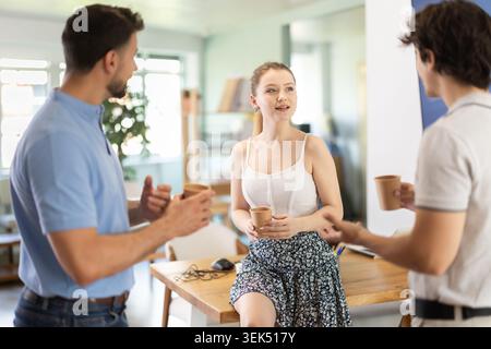 Two male and girl colleagues drink coffee and have nice conversation during break Stock Photo
