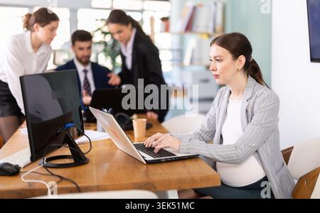Pregnant woman working on laptop in office Stock Photo