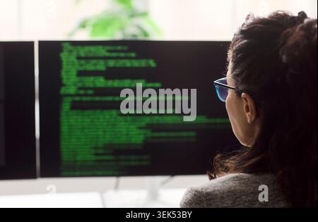 Rear view of female programmer reading code on dual monitors in modern office Stock Photo