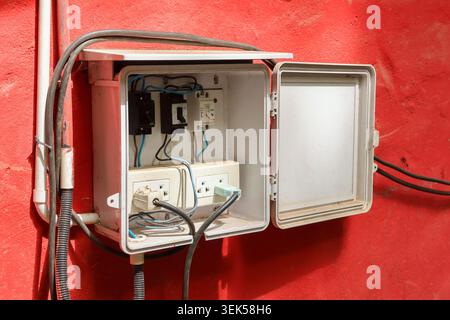 Open electrical panel box mounted on vivid red wall containing circuit breaker switches socket outlets power plugs connected cables providing reliable Stock Photo