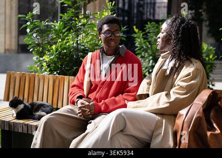 Relaxed african american couple man and woman sitting together on bench in park and talking Stock Photo