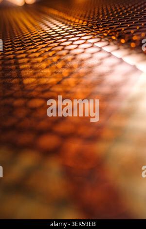 Vertical abstract background of perforated metal mesh with small holes in bright light orange color with shallow depth of field blurred bokeh texture. Stock Photo