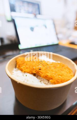Japanese-style breaded cutlet rice bowl in paper container on desk with laptop background Stock Photo