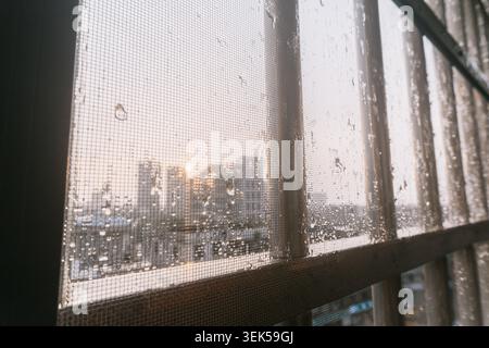 Raindrops on window screen with city skyline at golden hour sunset Stock Photo
