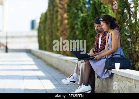Young couple working together on a laptop outdoors, collaborating and learning in a peaceful park setting Stock Photo