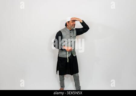 Indian man wearing traditional Islamic clothing, including a black cap (Kufi) and a waistcoat-style garment over a dark shirt and pants. He is gesturi Stock Photo