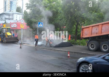 Construction workers are busy repairing the road surrounded by thick smoke and machinery. Kyiv, Ukraine, May 30, 2026 Stock Photo