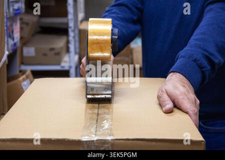 Warehouse worker sealing cardboard box with adhesive packaging tape and tape dispenser Stock Photo