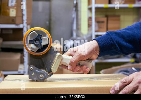 Close up view of hands sealing cardboard box with adhesive packaging tape and tape dispenser Stock Photo
