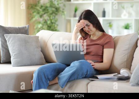 Young student suffering head ache e-learning sitting on a couch at home Stock Photo