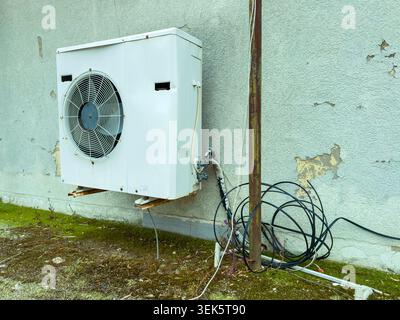 An air conditioning unit is installed on a wall with visible wires and connections nearby. The surface shows signs of wear and discoloration from the Stock Photo