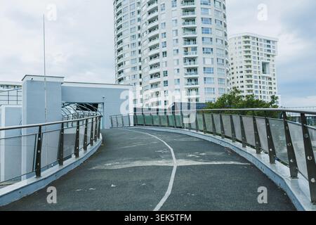 The scene shows a curved pathway leading to a building surrounded by tall structures. The gray sky adds to the city atmosphere during the day. Stock Photo