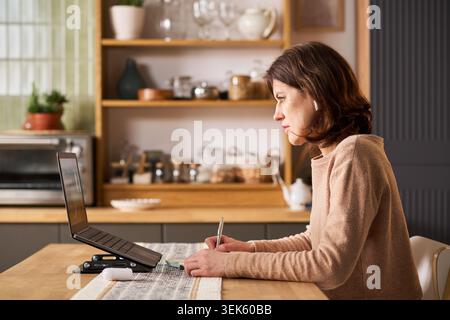 Middle Aged Woman Taking Remote Course Notes at Home Stock Photo