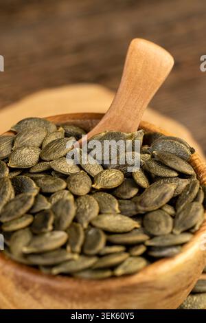 green large dried pumpkin seeds are lying on a wooden walnut board and in wooden dishes, a large number of healthy large pumpkin seeds without shells Stock Photo